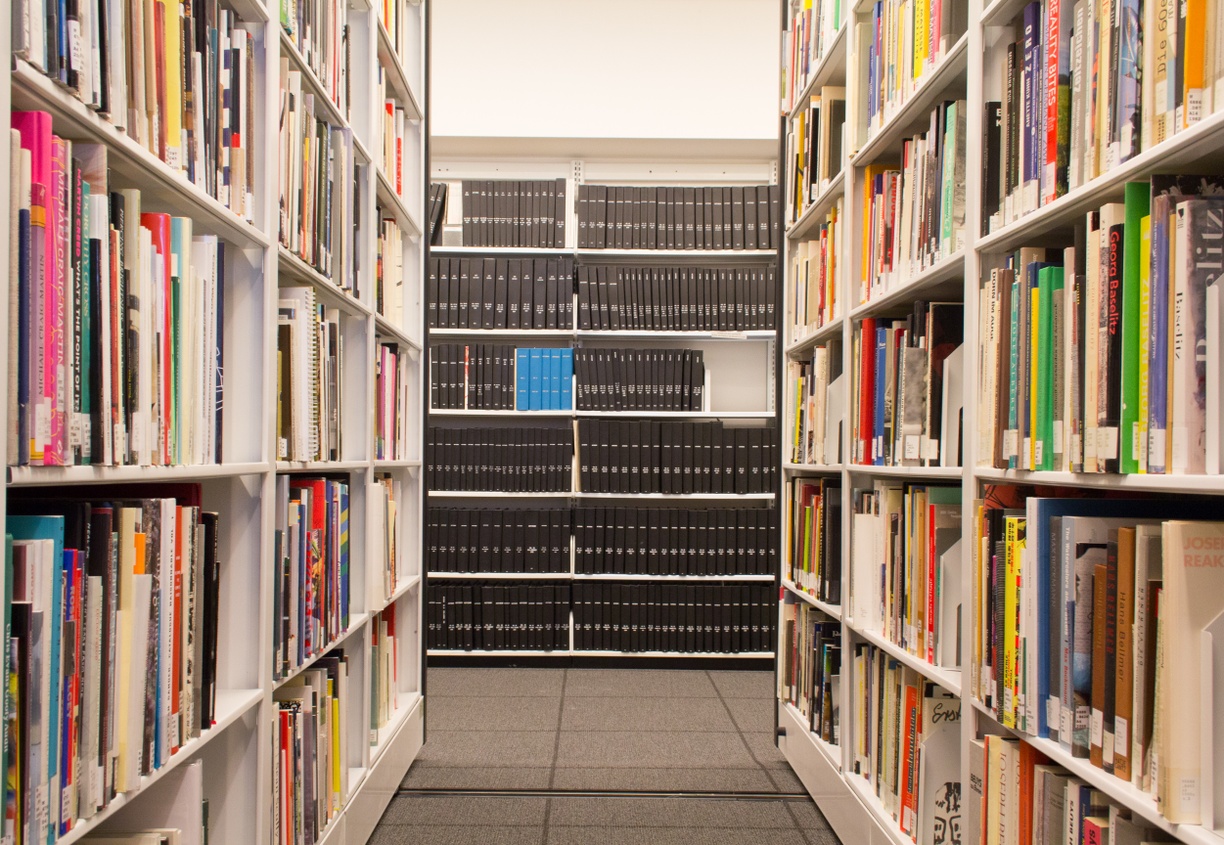 View down an aisle of books with bound periodicals on the bisecting wall.